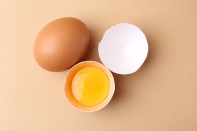 Photo of Whole and broken chicken eggs on beige background, top view
