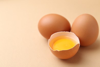 Photo of Whole and broken chicken eggs on beige background, closeup. Space for text