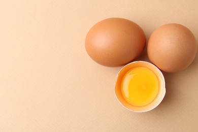 Photo of Whole and broken chicken eggs on beige background, top view. Space for text