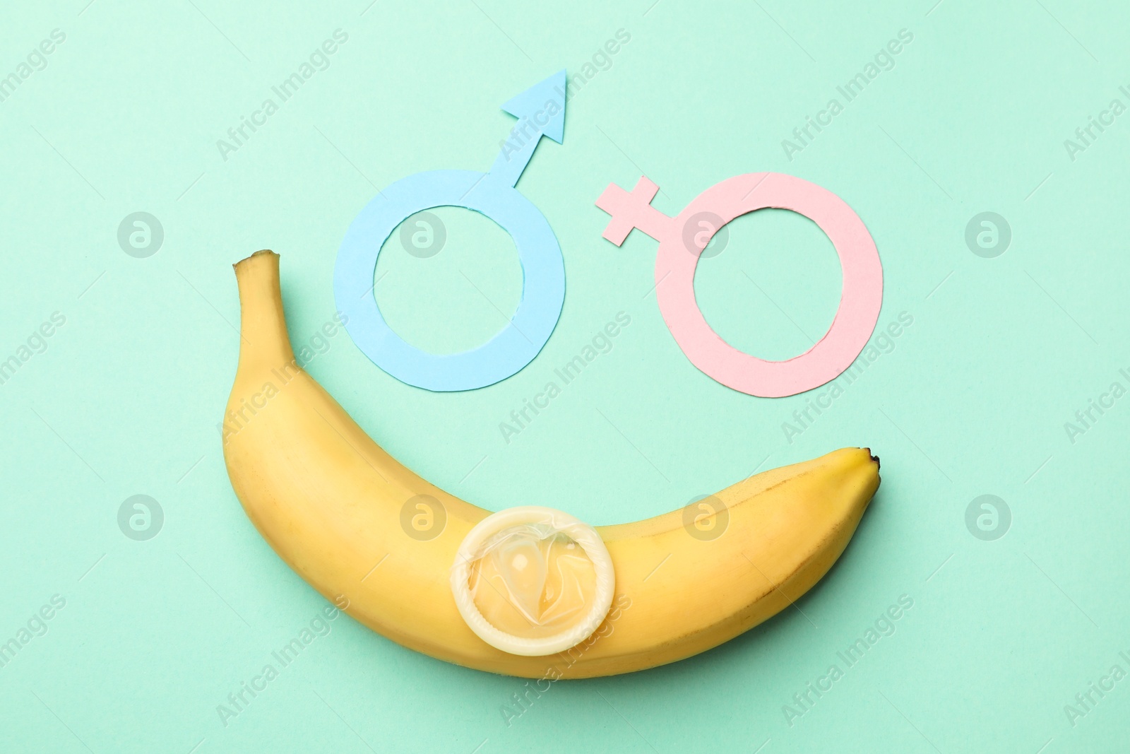 Sex education. Banana, condom, paper female and male gender symbols on turquoise background, flat lay Photo of Sex education. Banana, condom, paper female and male gender symbols on turquoise background, flat lay