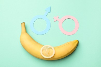 Photo of Sex education. Banana, condom, paper female and male gender symbols on turquoise background, flat lay