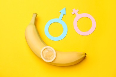 Photo of Sex education. Banana, condom, paper female and male gender symbols on yellow background, flat lay