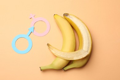 Photo of Sex education. Bananas, paper female and male gender symbols on pale orange background, flat lay