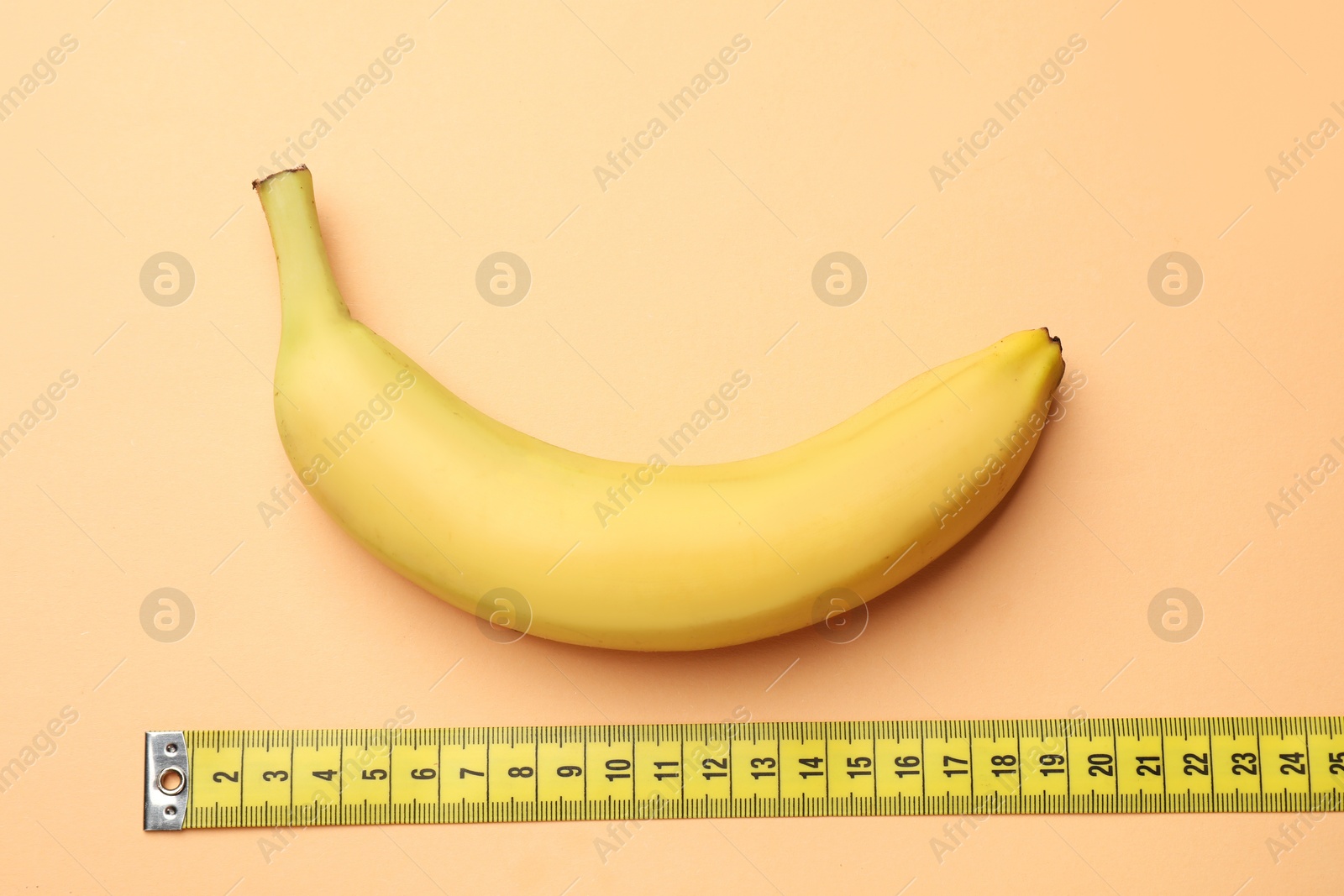 Sex education. Banana and measuring tape on pale orange background, flat lay Photo of Sex education. Banana and measuring tape on pale orange background, flat lay