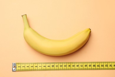 Photo of Sex education. Banana and measuring tape on pale orange background, flat lay