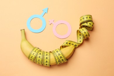 Photo of Sex education. Banana, measuring tape, paper female and male gender symbols on pale orange background, flat lay