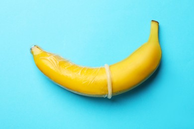 Photo of Sex education. Banana with condom on light blue background, top view