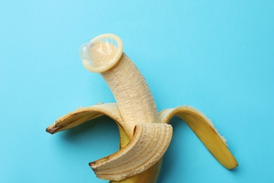 Photo of Sex education. Banana with condom on light blue background, top view