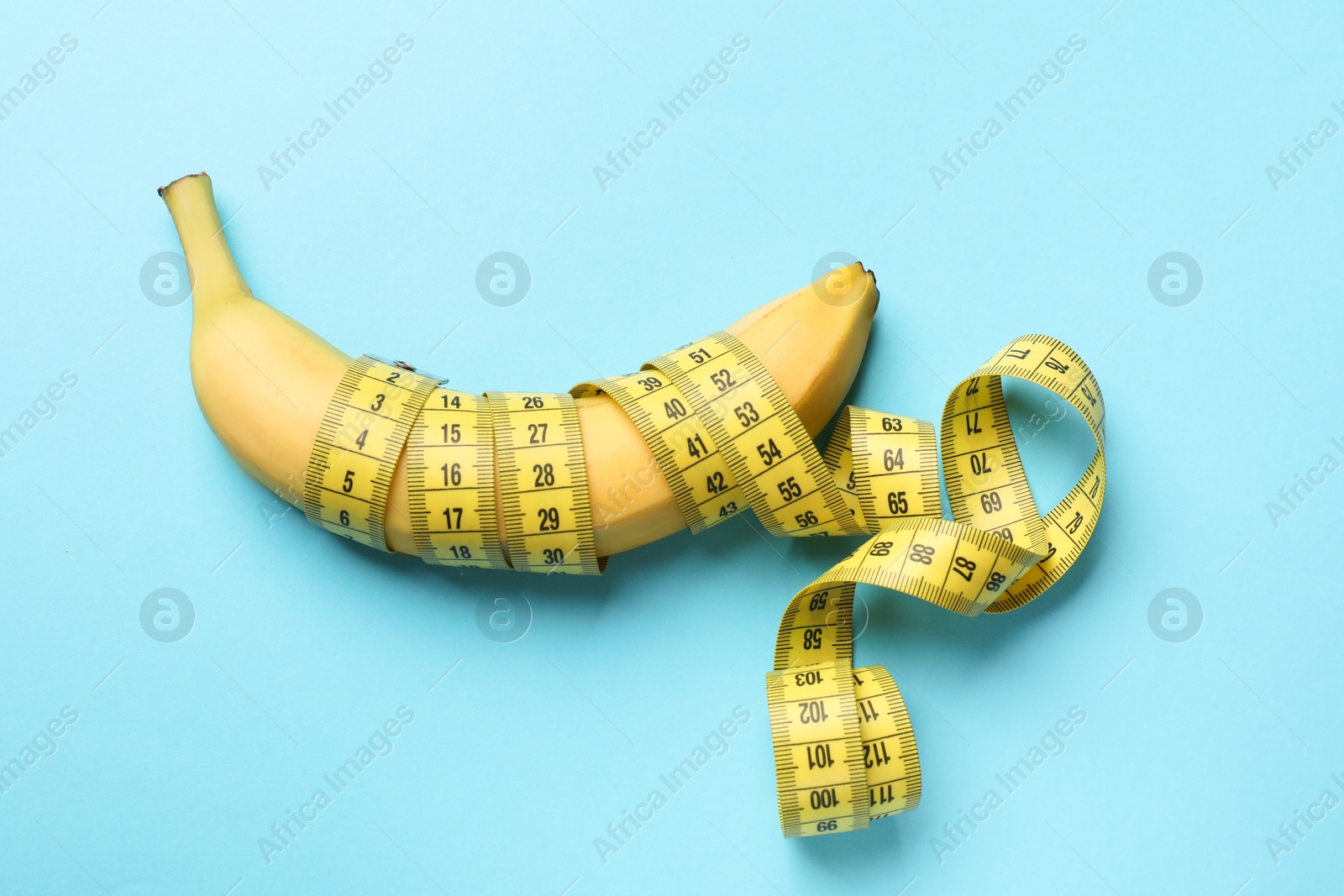 Sex education. Banana with measuring tape on light blue background, top view Photo of Sex education. Banana with measuring tape on light blue background, top view