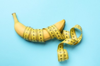 Photo of Sex education. Banana with measuring tape on light blue background, top view