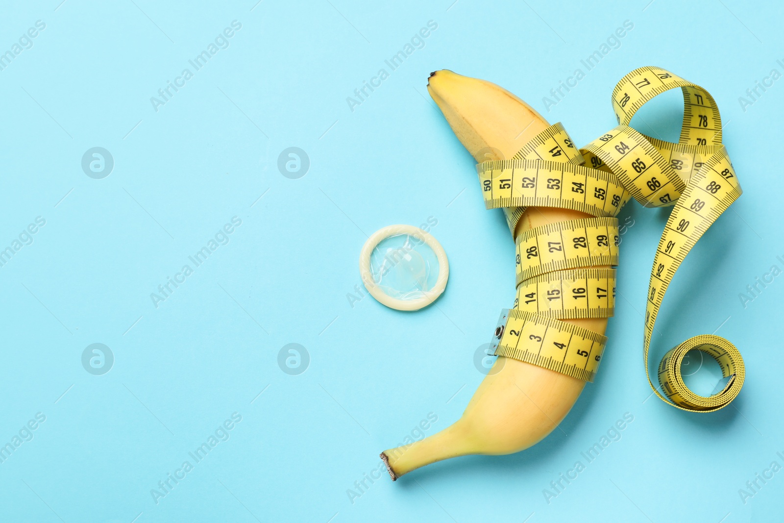 Sex education. Banana with measuring tape and condom on light blue background, flat lay. Space for text Photo of Sex education. Banana with measuring tape and condom on light blue background, flat lay. Space for text