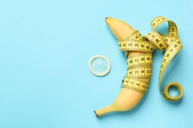 Photo of Sex education. Banana with measuring tape and condom on light blue background, flat lay. Space for text