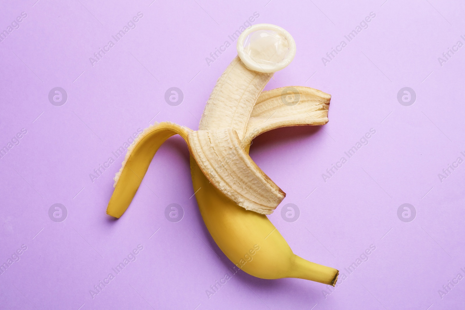 Sex education. Banana with condom on violet background, top view Photo of Sex education. Banana with condom on violet background, top view