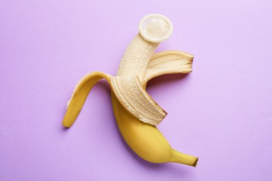 Photo of Sex education. Banana with condom on violet background, top view