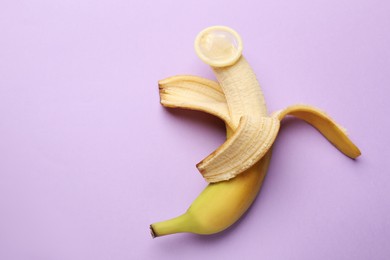 Photo of Sex education. Banana with condom on violet background, top view. Space for text