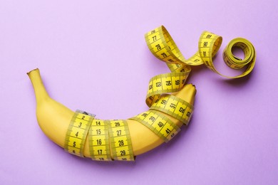 Photo of Sex education. Banana with measuring tape on violet background, top view