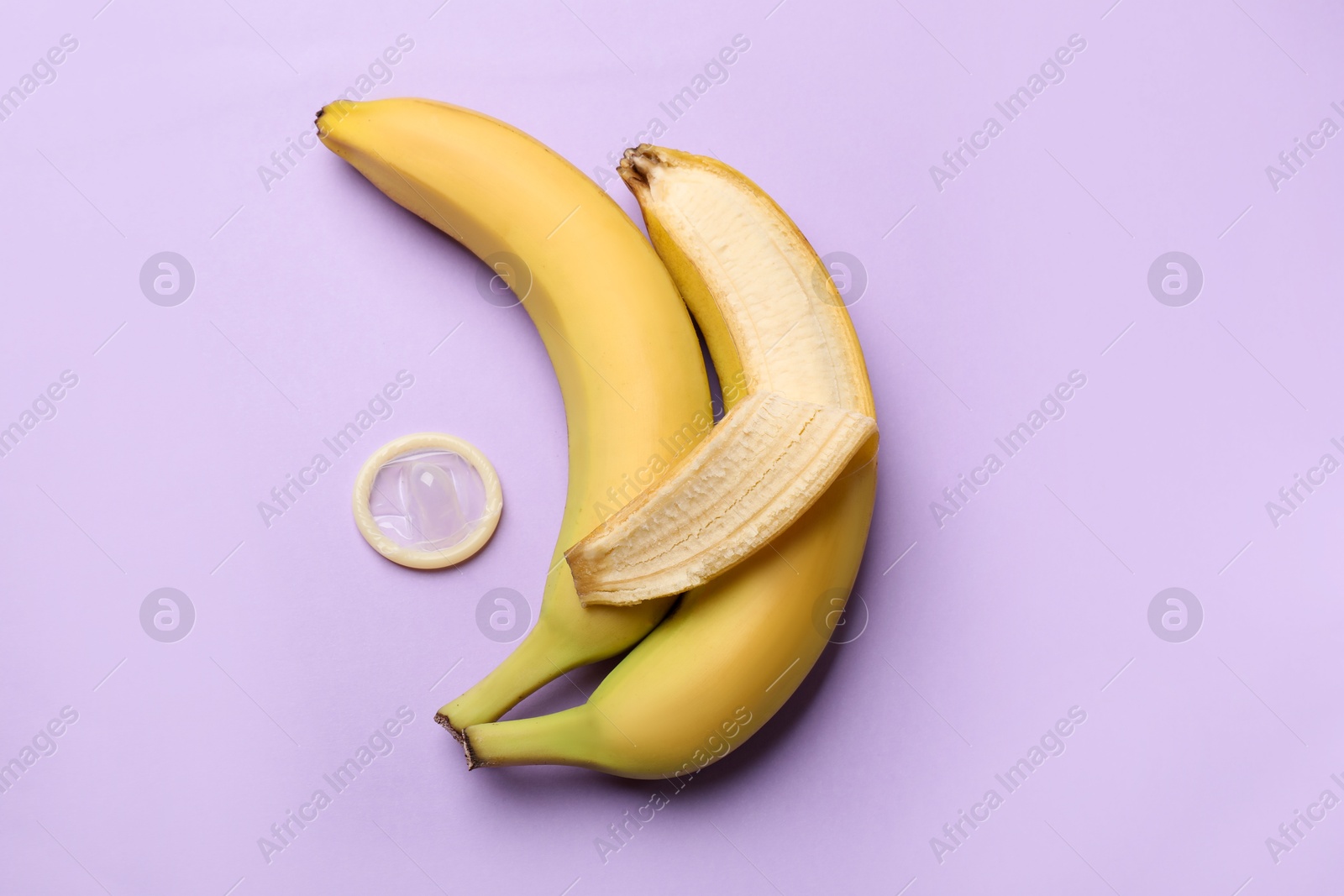 Sex education. Bananas with condom on violet background, flat lay Photo of Sex education. Bananas with condom on violet background, flat lay