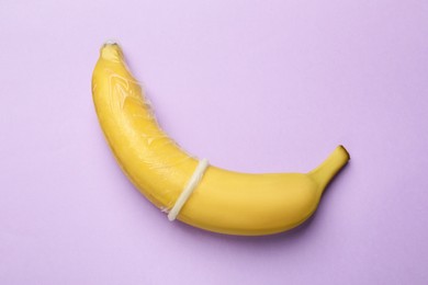 Photo of Sex education. Banana with condom on violet background, top view