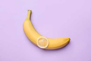 Photo of Sex education. Banana with condom on violet background, top view