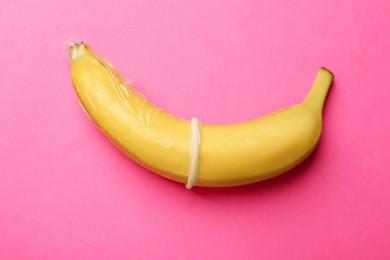 Photo of Sex education. Banana with condom on pink background, top view