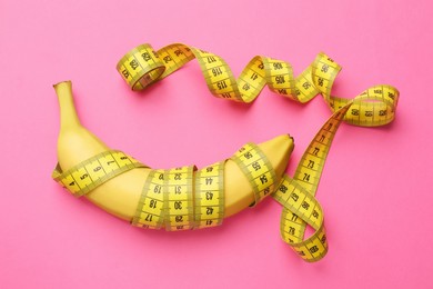 Photo of Sex education. Banana with measuring tape on pink background, top view