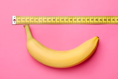 Photo of Sex education. Banana with measuring tape on pink background, flat lay