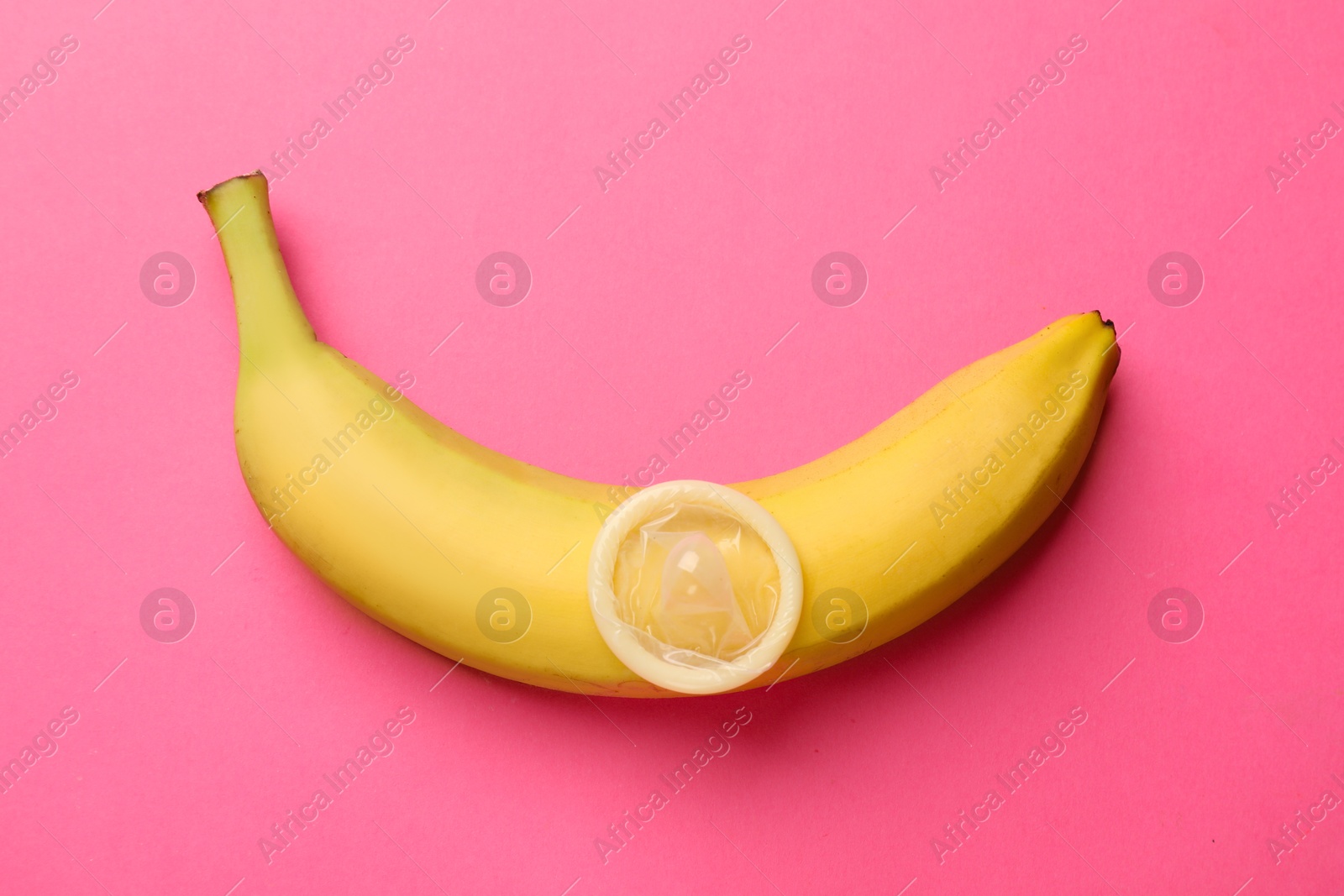 Sex education. Banana with condom on pink background, top view Photo of Sex education. Banana with condom on pink background, top view
