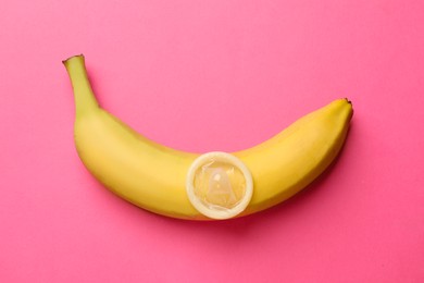 Photo of Sex education. Banana with condom on pink background, top view