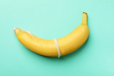 Photo of Sex education. Banana with condom on turquoise background, top view