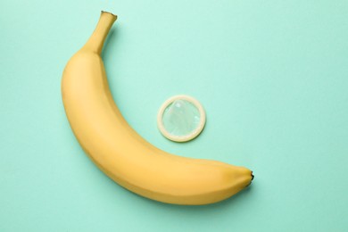 Photo of Sex education. Banana and condom on turquoise background, flat lay