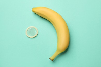 Photo of Sex education. Banana and condom on turquoise background, flat lay