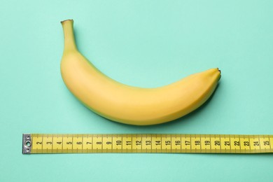 Photo of Sex education. Banana with measuring tape on turquoise background, flat lay