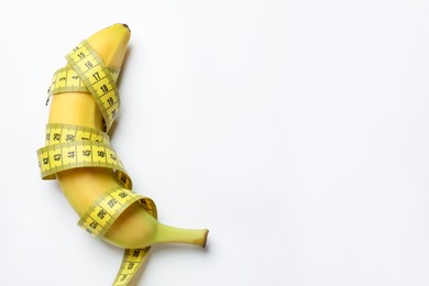 Photo of Sex education. Banana with measuring tape on white background, top view. Space for text