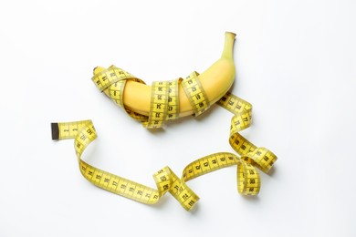 Photo of Sex education. Banana with measuring tape on white background, top view