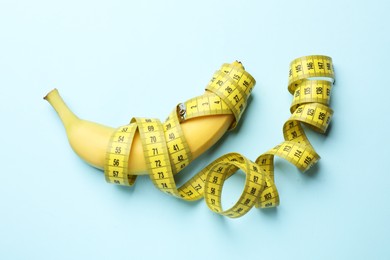 Photo of Sex education. Banana with measuring tape on light blue background, top view