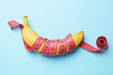 Photo of Sex education. Banana with measuring tape on light blue background, top view