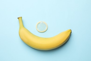 Photo of Sex education. Banana and condom on light blue background, flat lay