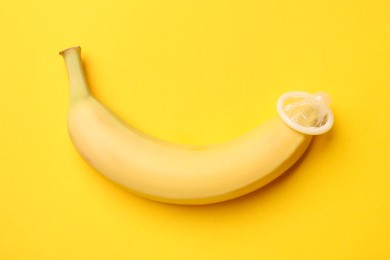 Photo of Sex education. Banana with condom on yellow background, top view