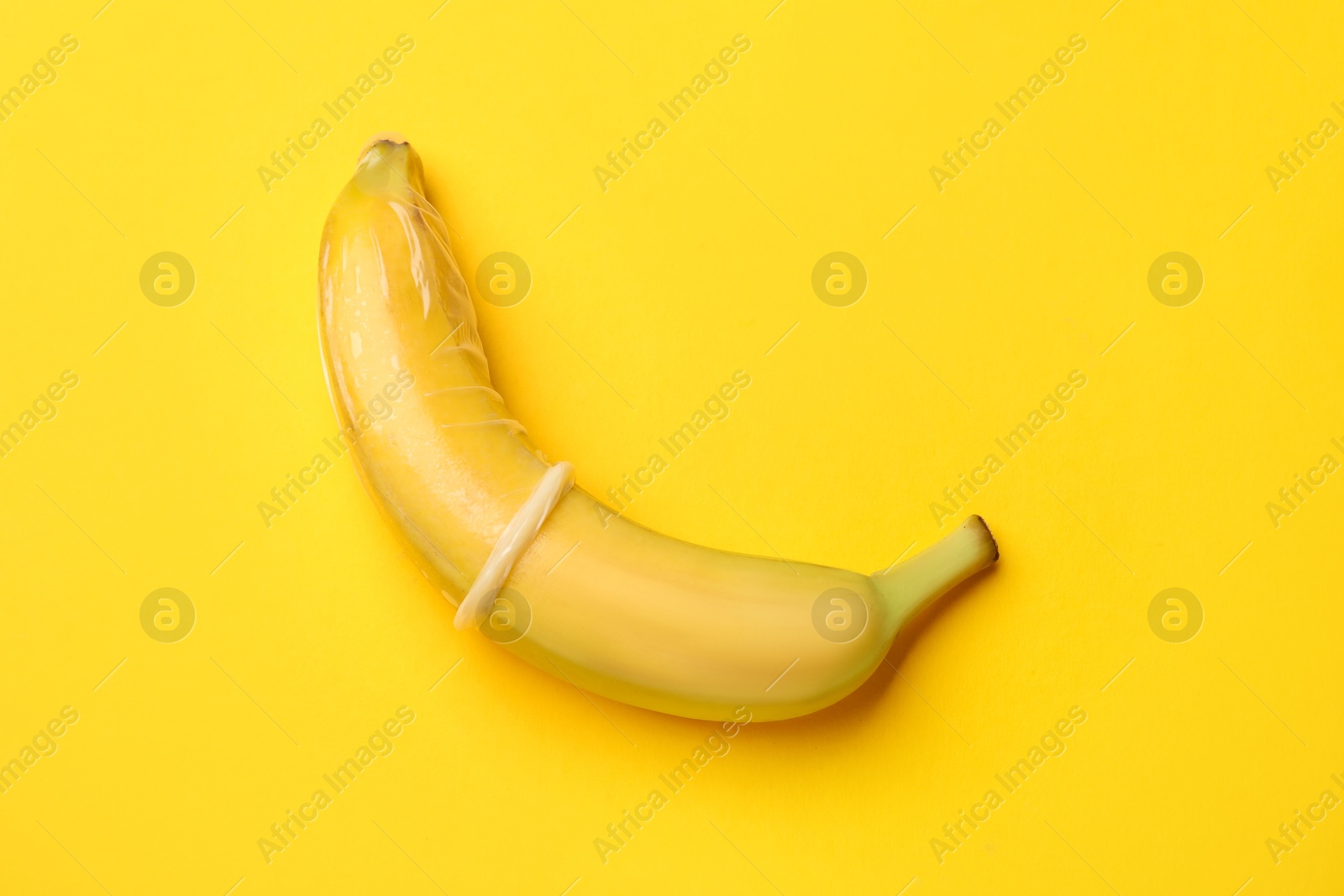 Sex education. Banana with condom on yellow background, top view Photo of Sex education. Banana with condom on yellow background, top view