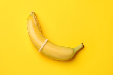 Photo of Sex education. Banana with condom on yellow background, top view