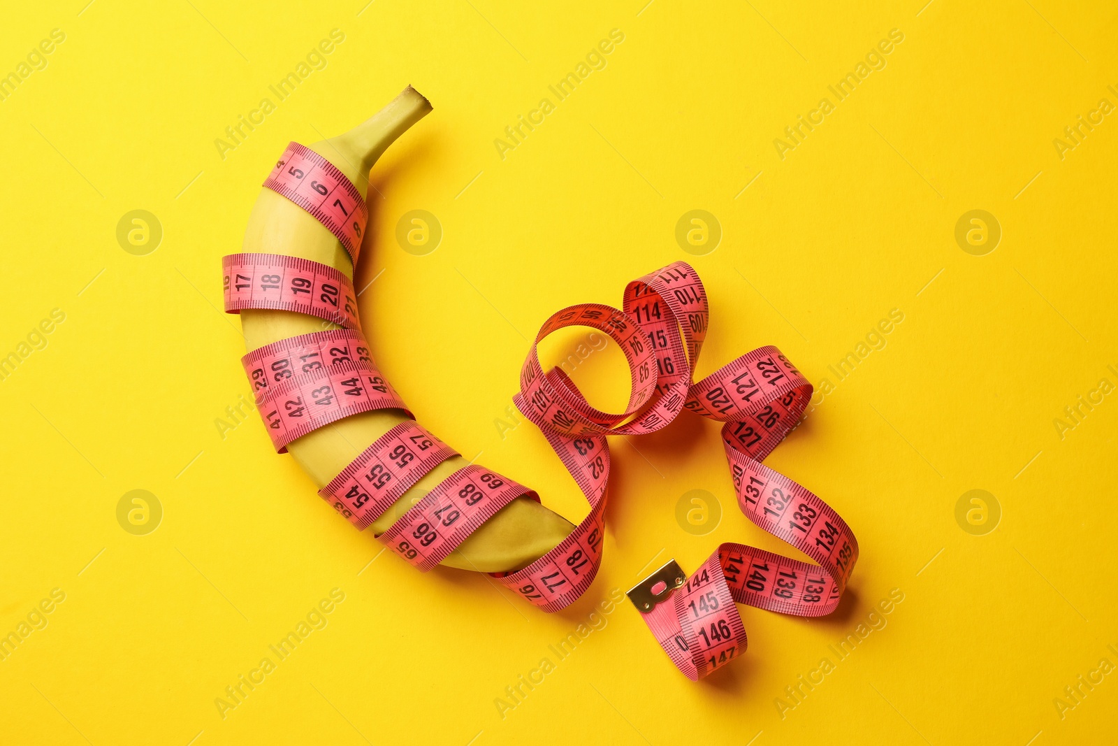 Sex education. Banana with measuring tape on yellow background, top view Photo of Sex education. Banana with measuring tape on yellow background, top view