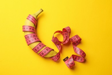 Photo of Sex education. Banana with measuring tape on yellow background, top view