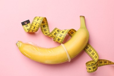 Photo of Sex education. Banana with measuring tape and condom on pink background, top view