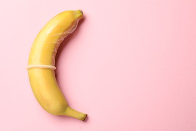 Photo of Sex education. Banana with condom on pink background, top view. Space for text
