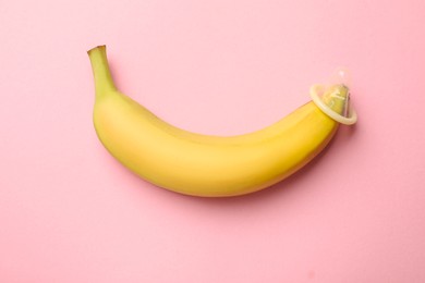 Photo of Sex education. Banana with condom on pink background, top view