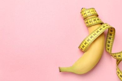 Photo of Sex education. Banana with measuring tape on pink background, top view. Space for text