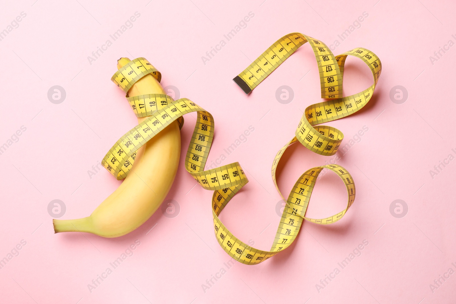 Sex education. Banana with measuring tape on pink background, top view Photo of Sex education. Banana with measuring tape on pink background, top view