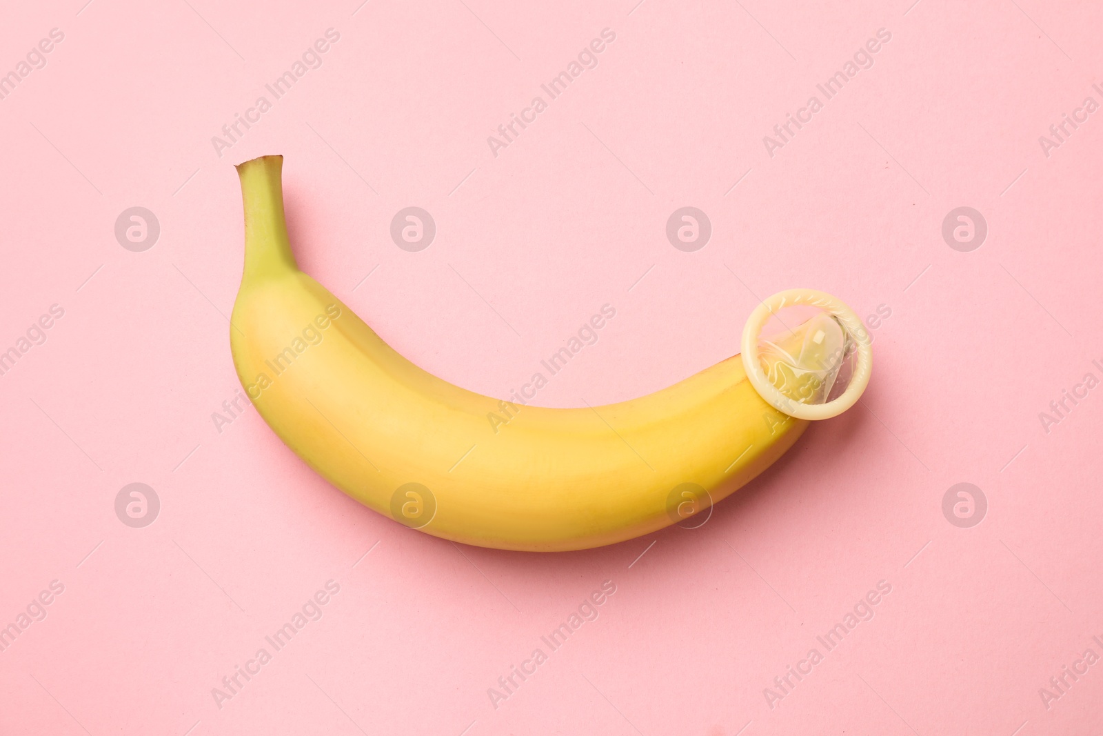 Sex education. Banana with condom on pink background, top view Photo of Sex education. Banana with condom on pink background, top view