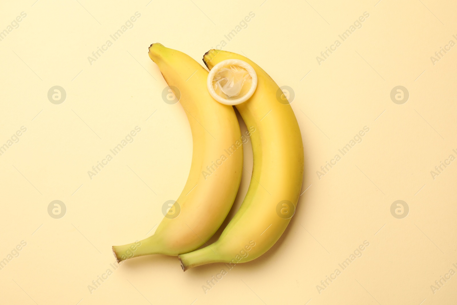Sex education. Bananas with condom on beige background, flat lay Photo of Sex education. Bananas with condom on beige background, flat lay