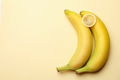 Photo of Sex education. Bananas with condom on beige background, flat lay. Space for text